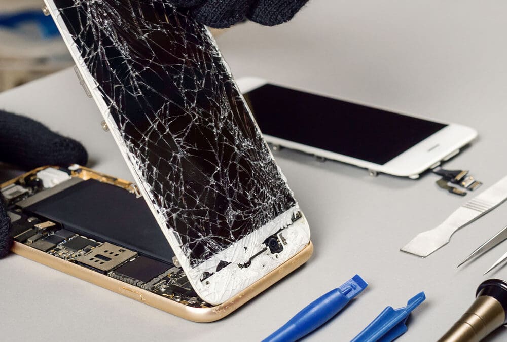 Technician repairing a smartphone with a shattered screen using precision tools