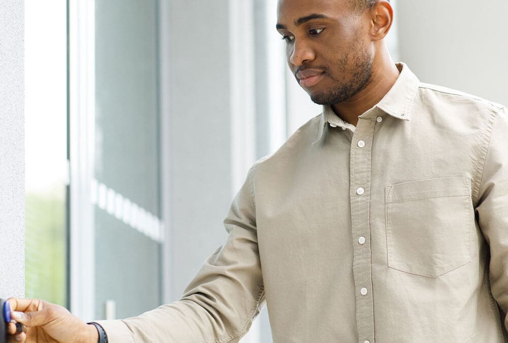 Employee holding a credential to a wall-mounted access control reader beside an office door